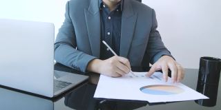 一个穿着正装的聪明的商人，在办公桌上用笔记本电脑和数据图表信息工作，展示了在数据分析，营销和金融方面的职业生涯概念。