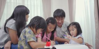 幸福的亚洲家庭和他们的三个女儿在家里的客厅里用彩色铅笔画画。