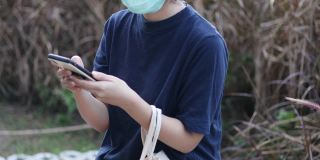 亚洲女性戴着防护面具在户外花园玩智能手机放松