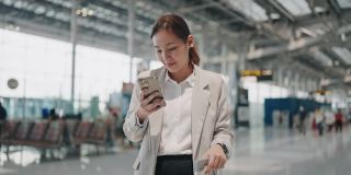 微笑的年轻亚洲女人在机场使用智能手机