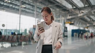微笑的年轻亚洲女人在机场使用智能手机视频素材模板下载