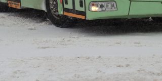 冬天。公共城市交通巴士正行驶在城市的雪道上。用慢动作对车轮轮胎进行特写。降雪。交通状况不佳，暴风雪。有发生交通事故的危险。十字路口