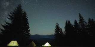 在星星闪烁的夜空下，山间树林中露营地的游客帐篷旁，明亮的篝火旁，徒步旅行者在休息。积极的生活方式和户外生活理念