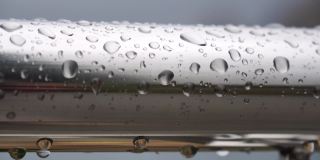 不锈钢扶手上的雨滴映衬着模糊的大海背景。特写镜头。雨露的水滴聚集在闪闪发光的铬钢杆扶手上