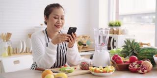 亚洲高级妇女在准备用不同的口味和酸奶自制水果冰沙时感到幸福。健康天然益生菌调味饮料，在厨房学习使用科技