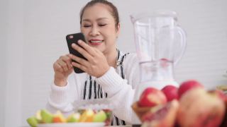 亚洲资深女性网红，一边教如何自制不同口味和酸奶的水果冰沙，一边查看粉丝。健康天然益生菌调味饮品，在厨房学习使用科技，低角度视角。视频素材模板下载