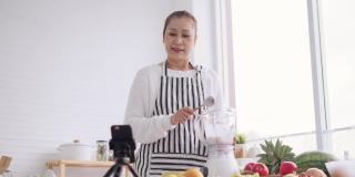 亚洲资深女性作为影响者，教如何制作自制的水果冰沙与不同的口味和酸奶。健康天然益生菌调味饮料，学会使用科技，在厨房用智能手机与观众交谈，低角度