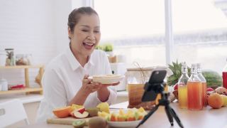 亚洲资深女性影响者教授如何制作自制的发酵生康普茶与不同的口味。健康天然益生菌调味饮料，学会使用科技，在厨房用智能手机与观众交谈，侧视视频素材模板下载