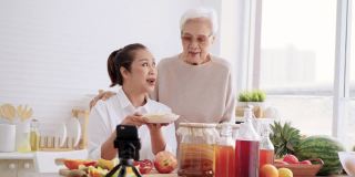 亚洲年长的女儿和母亲作为影响教授如何自制发酵生康普茶与不同的口味。健康的天然益生菌口味饮料，学习使用科技，在厨房用智能手机与观众交谈