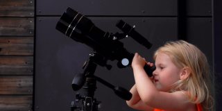 一个穿橙色上衣的小女孩正在通过望远镜探索天空