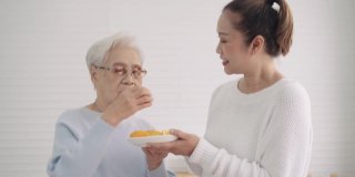 中女儿让她的亚洲年长的母亲在厨房准备水果奶昔之前尝一小块橘子，享受周末的活动，前面的景象，年长的生活方式