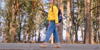 搭便车旅行的概念。一名年轻的女游客背着黄色夹克的背包，手里拿着保温瓶，沿着松树林走着。有选择性的重点。慢镜头,4 k