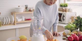 亚洲老年女性，80岁，用电动搅拌机自己准备水果奶昔，享受周末活动与健康饮食，侧视，城市生活的老年人生活方式，退休后独自一人的人