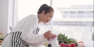 亚洲高级妇女准备自制水果冰沙与不同的口味，草莓，石榴，橘子和酸奶。健康的天然益生菌调味饮料，侧视
