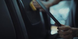 在汽车详细清洁服务期间，一位年轻人在清洁座椅坐垫时使用精细的布对汽车内部进行深层清洁。