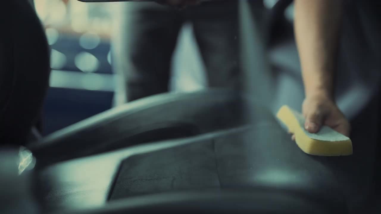 在汽车详细清洁服务期间，一位年轻人在清洁座椅坐垫时使用精细的布对汽车内部进行深层清洁。