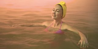 靠近白种人女子在热盐水矿泉浴在一个传统的温泉室外柔和的魔术粉红色照明蒸汽。地热温泉。