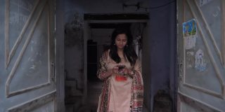 一位印度传统的快乐微笑的妇女走在一条狭窄的巷子里用手机发短信