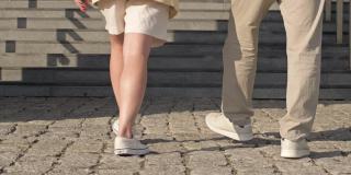 男女脚在舒适的休闲鞋上跑楼梯。成熟的夫妇很容易爬上石阶。后视图