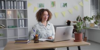 远程培训，一个戴眼镜的成年女孩的肖像，通过在笔记本电脑上的视频交流与老师在线远程授课，在笔记本上写微笑和看着相机