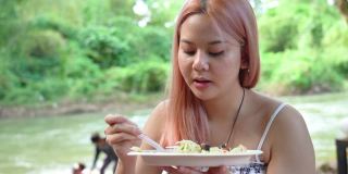 周末，年轻的亚洲女游客在海滨吃着辣木瓜沙拉