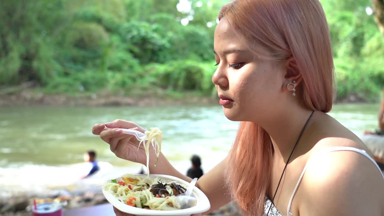 周末，年轻的亚洲女游客在海滨吃着辣木瓜沙拉