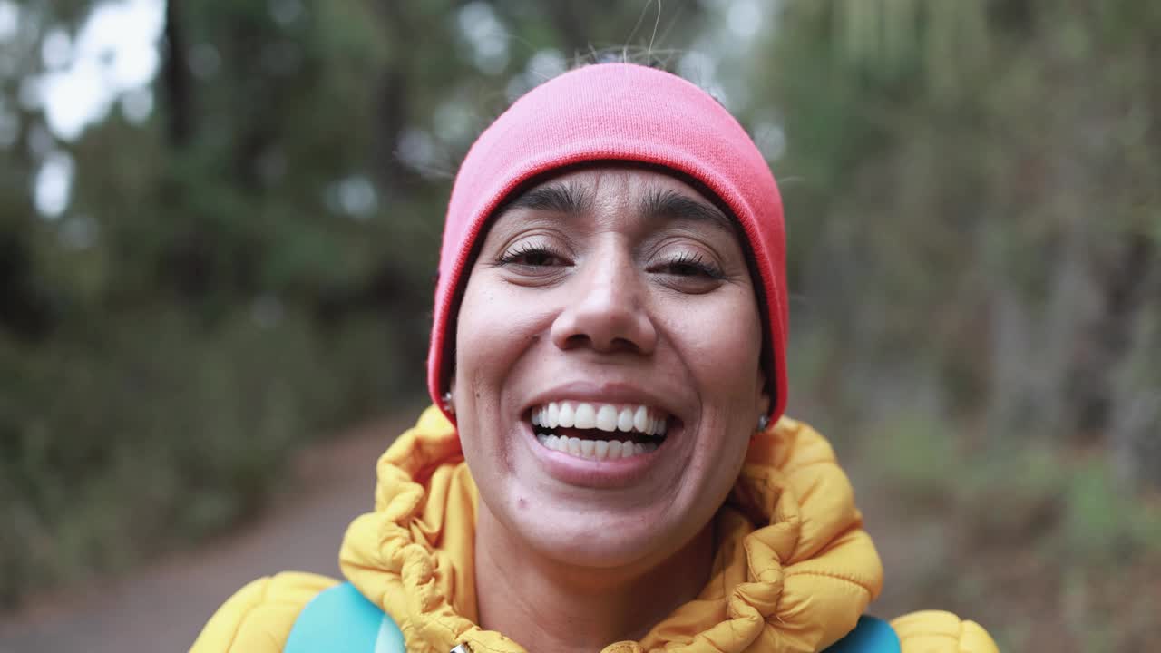 一位年轻的拉丁女子在森林里徒步行走时，对着镜头微笑