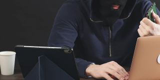 戴着黑色面罩的男性黑客用笔记本电脑黑进了硬盘