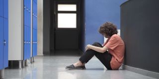 悲伤的少年学生独自坐在地板上欺凌的受害者和友好的同学朋友帮助和安慰他。教育中的同理心和支持