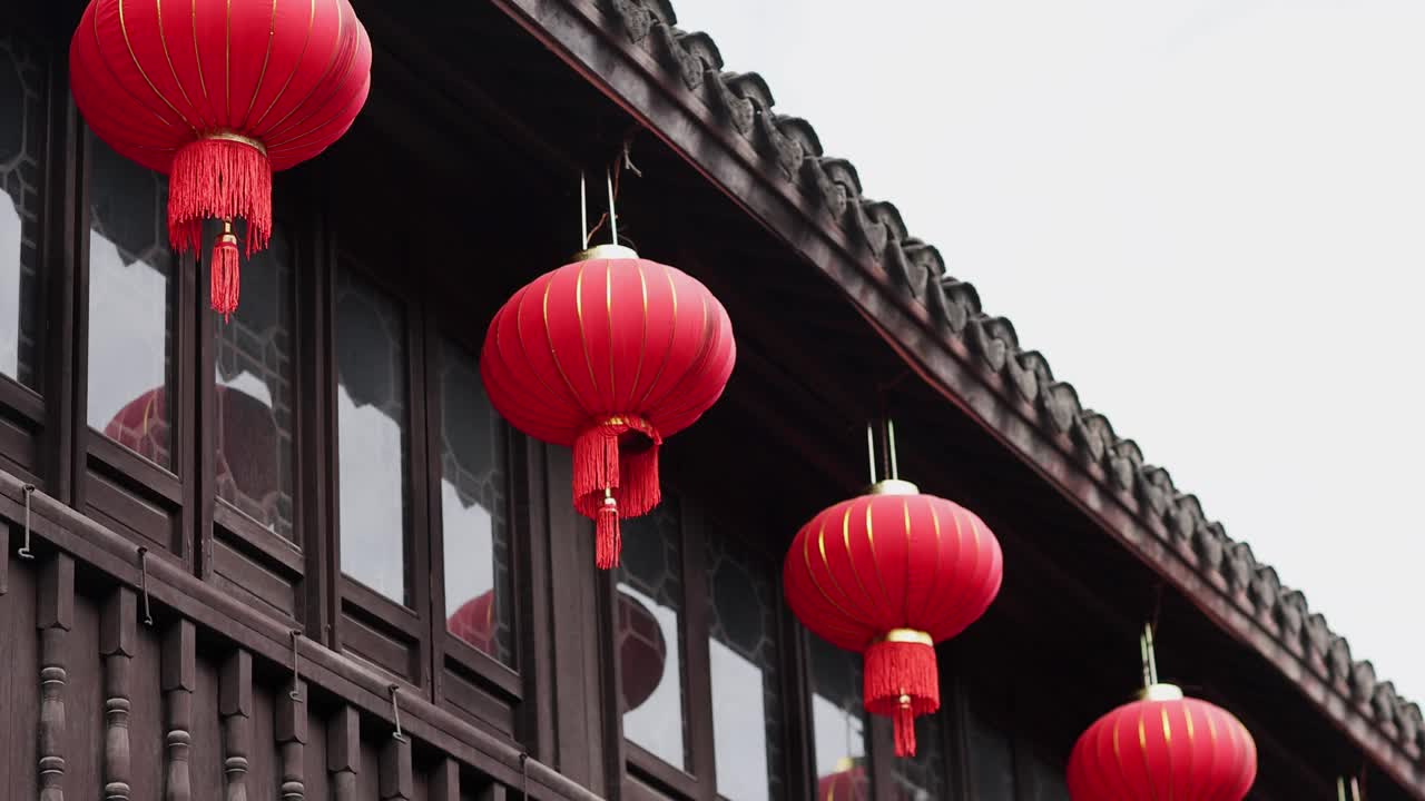 中国古老的传统建筑，用红灯笼装饰以庆祝中国新年或春节。屋顶上的东方纸灯随风摇曳。慢动作