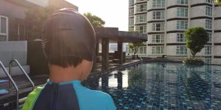 小男孩站在公寓游泳池边上准备跳下去锻炼。