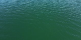 无缝的无人机视野在碧绿的湖水涟漪接近。鸟瞰图的海或海洋与美丽的波浪图案的景观，无尽的海蓝宝石水在夏天的日子。