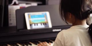 亚洲女孩正在学习和练习钢琴音乐使用在线平板电脑应用程序连接键盘使用蓝牙。