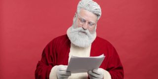 圣诞老人快乐，圣尼古拉斯阅读愿望信，检查孩子梦想的礼物清单。他高兴、满足、幸福。红色的背景