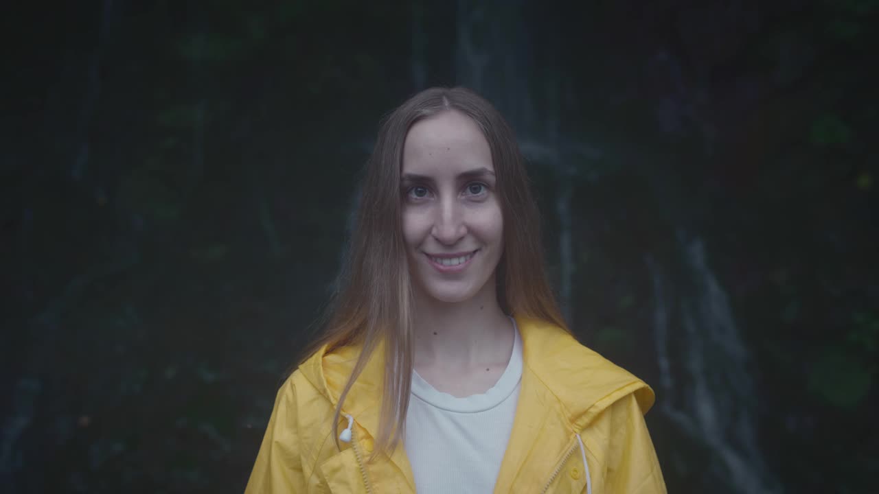 白种人女孩的肖像旅行者在森林瀑布附近的黄色雨衣。生活方式的概念，慢动作