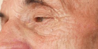一个忧郁的老人的特写镜头。70岁以上的老年白人男性的眼睛有皱纹。生活经验。领养老金的人思考人生。选择性对焦，景深浅