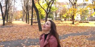 年轻女子在秋天的公园里抛起枯叶，快乐少女