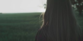 黄昏或黎明时分，一个身穿红色格子衬衫的年轻女孩站在田野里。头发被风吹着