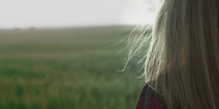 黄昏或黎明时分，一个年轻浪漫的女孩身穿红色格子衬衫站在田野里。头发被风吹着