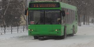 冬天。公共城市交通巴士正行驶在城市的雪道上。慢动作降雪。交通状况不佳，暴风雪。有发生交通事故的危险。十字路口