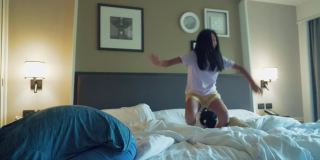 微笑的亚洲女孩跳酒店的床在假期，生活方式的概念。