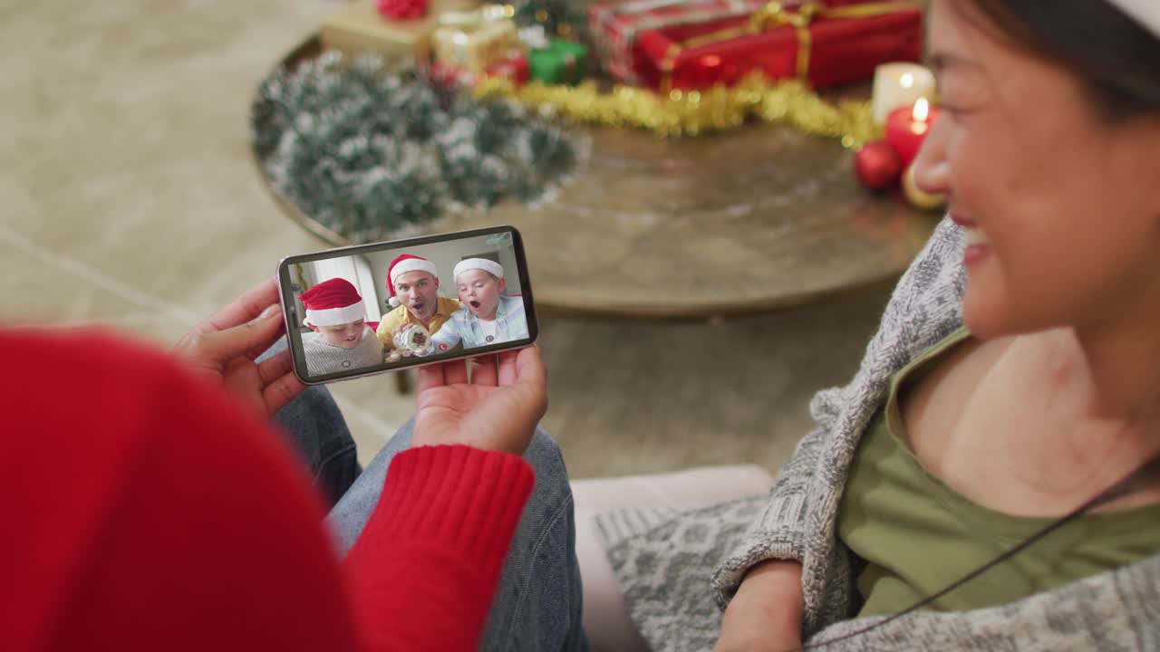 微笑的亚洲夫妇用智能手机与屏幕上的圣诞老人帽子的家人进行圣诞视频通话