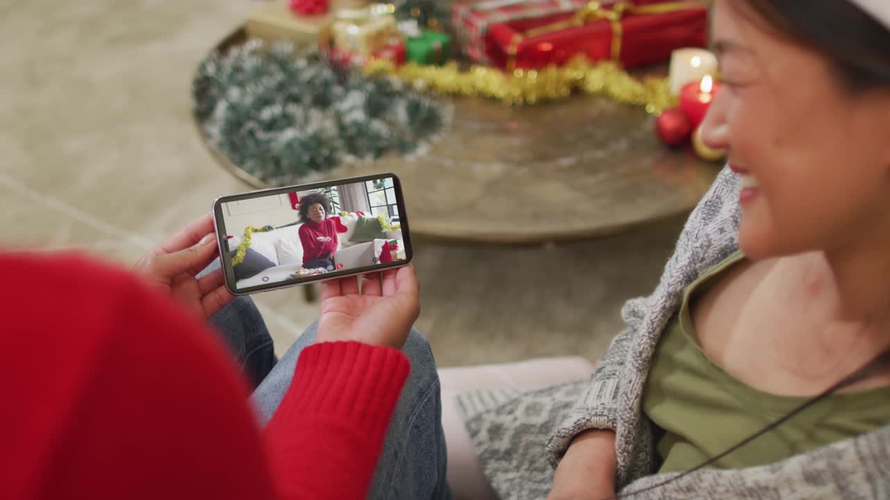 一对微笑的亚洲夫妇用智能手机与屏幕上戴着圣诞老人帽子的女人进行圣诞视频通话