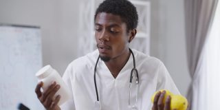 专业医生拿着药物和柠檬拉伸有机维生素水果看着镜头。严肃自信的非洲裔美国人提供替代治疗而不是药物治疗。选择的概念。
