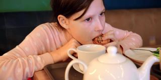 快乐的女孩在咖啡厅喝茶，吃蛋糕马卡龙。十几岁的女孩坐在桌子和吃在咖啡厅里面。爱吃甜食的孩子吃美味的蛋糕。