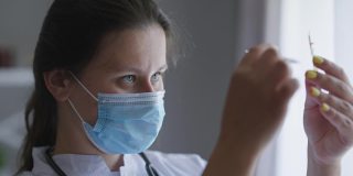 照片中的护士戴着冠状病毒口罩在室内检查药品安瓿。集中高加索年轻美丽的医生科学家寻找治疗新冠病毒大流行。