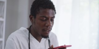 被爆头的非裔美国医生正在用智能手机录制语音邮件。专家，聪明的人在电话上在线聊天。生活方式和现代科技的便利。