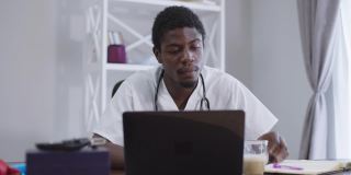 前面的观点集中在聪明的非洲裔美国医生喝早上的咖啡，在室内用笔记本电脑上网。一个精力集中聪明的年轻人坐在医院的桌子旁阅读在线新闻。