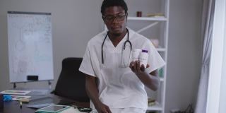 自信微笑的非洲裔美国医生戴着眼镜，竖起大拇指，看着广告维生素的照相机。年轻聪明的人的肖像与白板与化学公式的背景。