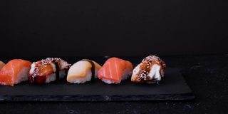黑色的盘子上放有三文鱼、鳗鱼和鲱鱼的什锦寿司，背景为黑色。最小的概念